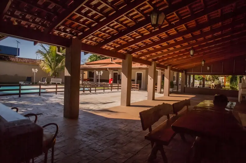 Área coberta com mesas de madeira rústica e vista para a piscina no fim da tarde