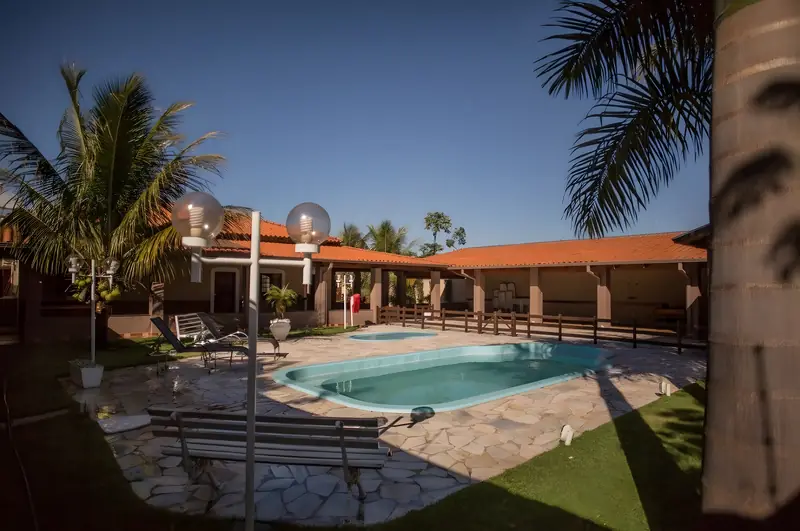 Área da piscina com luminárias de globo, deque de pedra, palmeiras e as varandas ao fundo