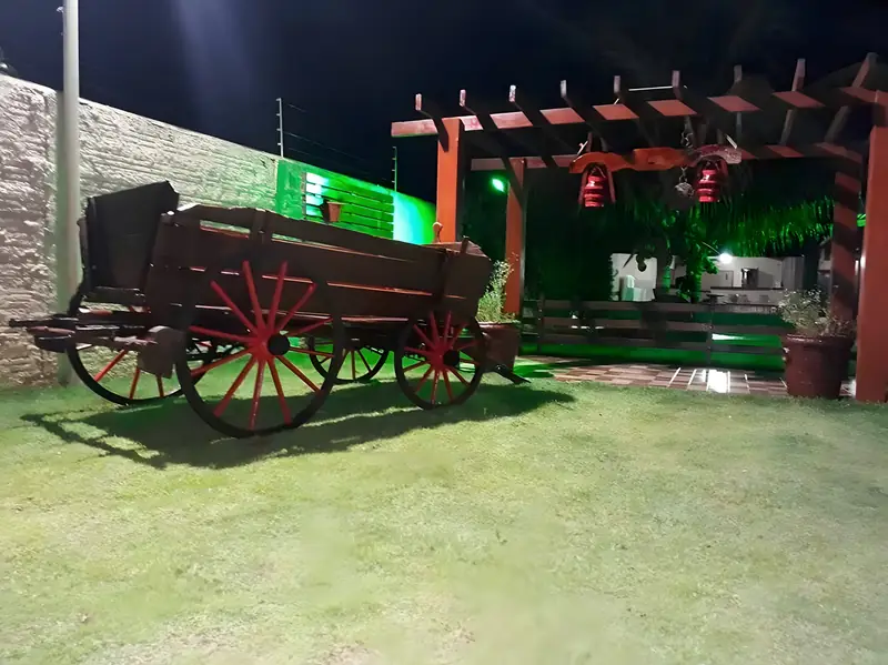 Carro de boi decorativo e pérgola no jardim iluminado à noite