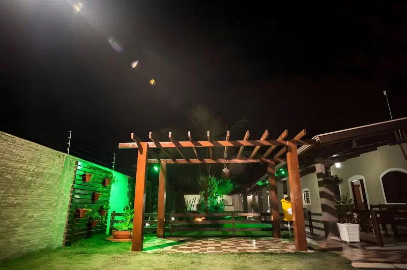 Pérgola de madeira iluminada à noite, junto à varanda da casa
