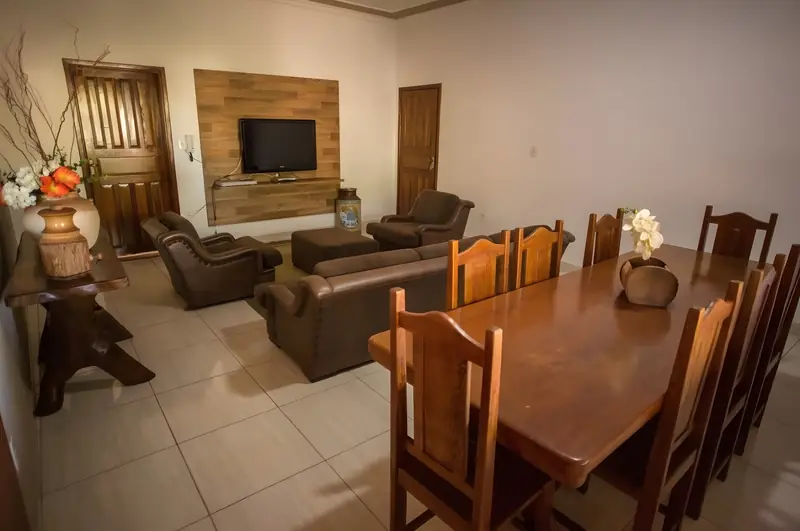 Sala com sofás de couro, mesa de jantar de madeira com cadeiras e TV