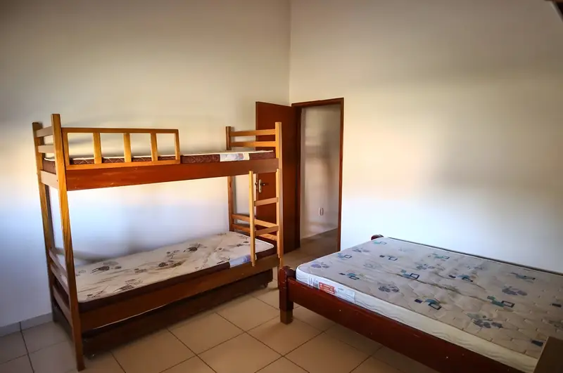 Suíte com beliche de madeira, cama de casal e porta do banheiro