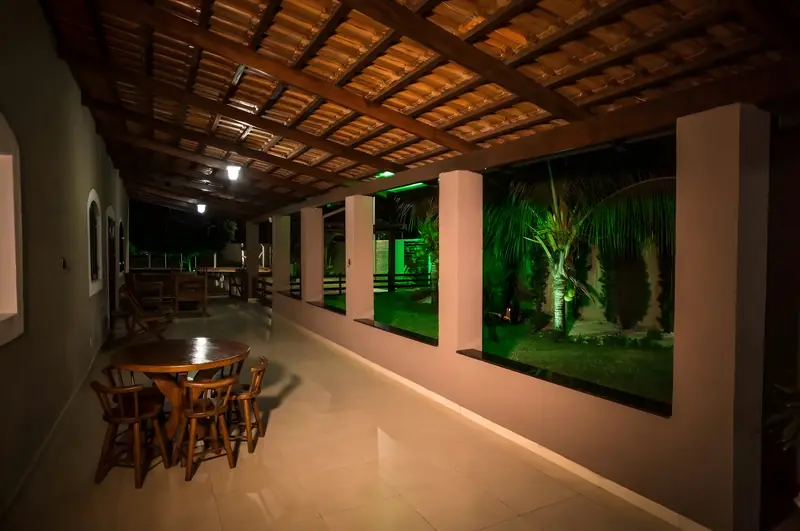 Varanda coberta com mesas de madeira e o jardim iluminado à noite